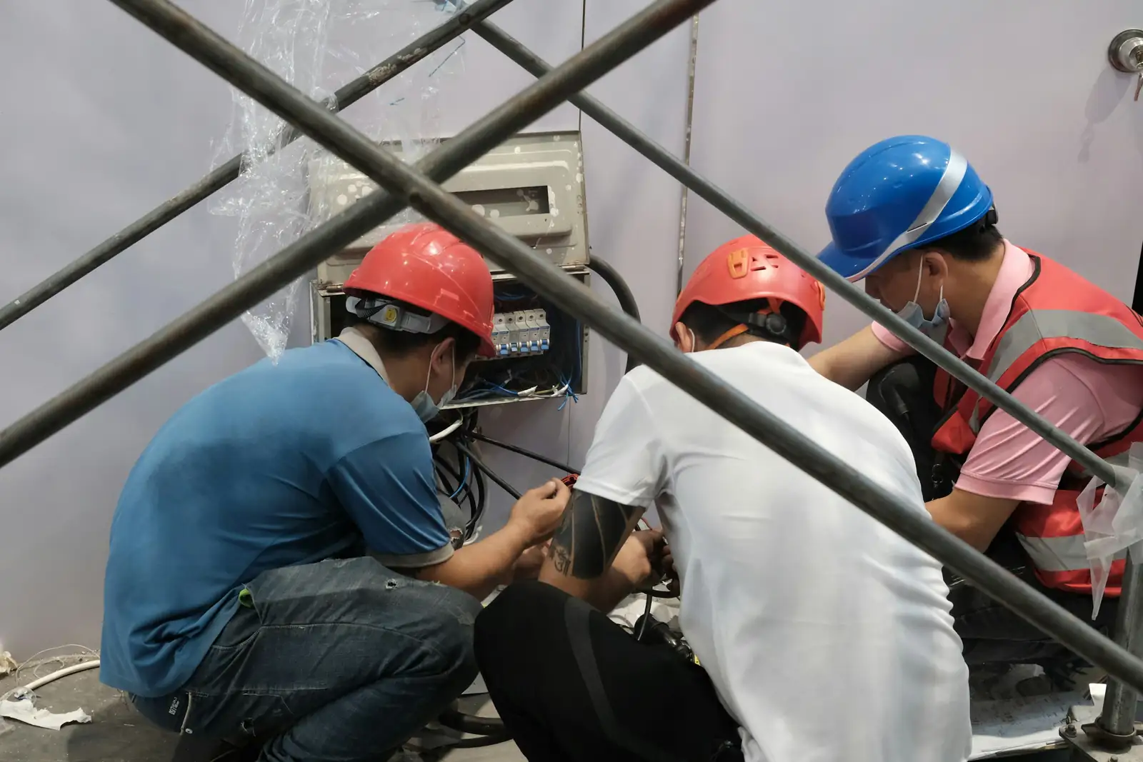 Teknisi berhelm merapikan instalasi listrik booth di balik rangka scaffolding