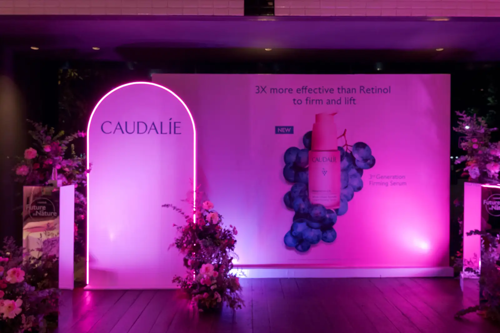 Backdrop peluncuran Caudalie Resveratrol-Lift dengan lengkung bercahaya merah muda dan rangkaian bunga