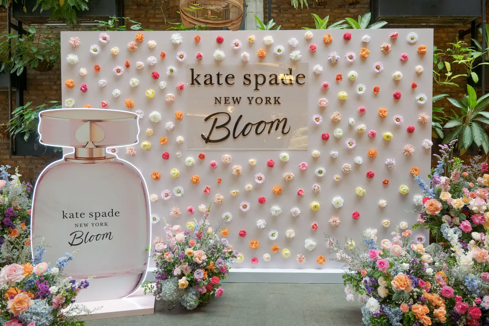 Dinding bunga Kate Spade Bloom dengan replika botol parfum besar dan rangkaian bunga di Blue Jasmine