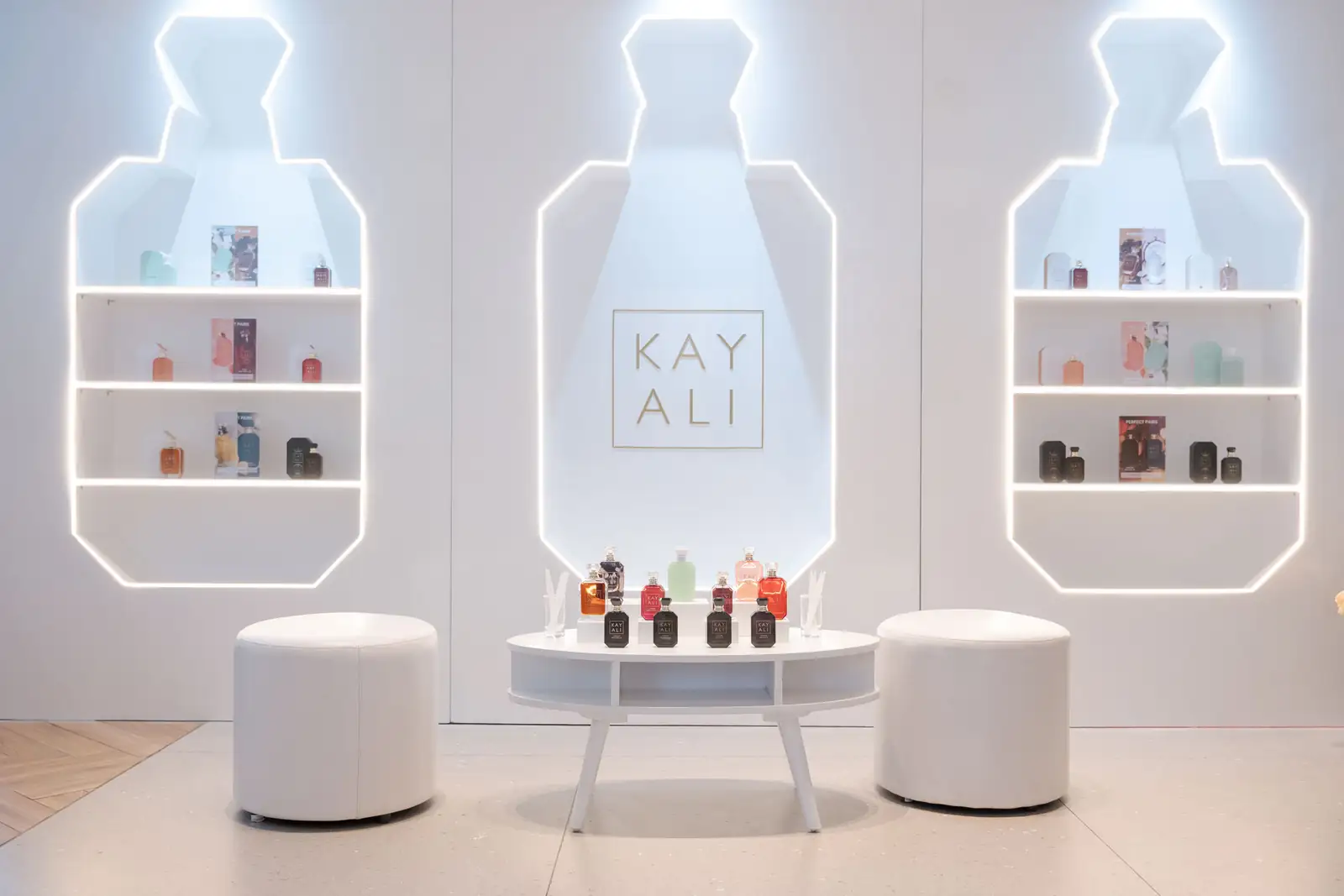Instalasi putih KAYALI berbentuk botol parfum bercahaya dengan rak display di La Gazette, Jakarta